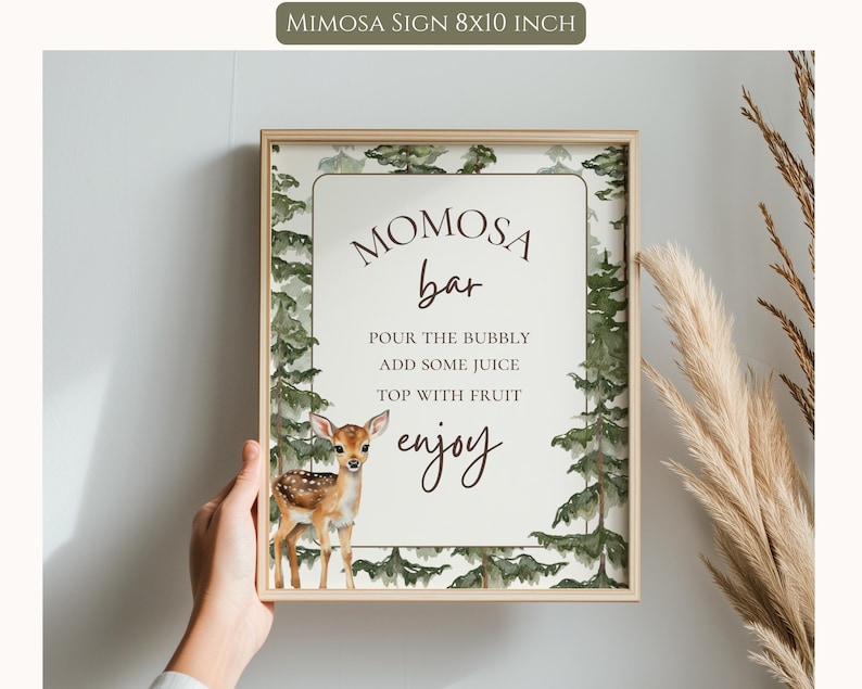 May include: A rectangular 8x10 inch sign in a light wood frame featuring a watercolor forest border with green pine trees and a small brown fawn. The text reads: MOMOSA bar, POUR THE BUBBLY, ADD SOME JUICE, TOP WITH FRUIT, enjoy.