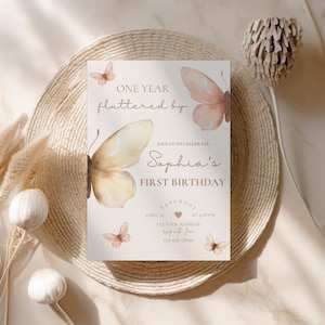 Pode incluir: Um cartão de convite bege com ilustrações de borboletas e o texto "ONE YEAR fluttered by" e "Sophia's FIRST BIRTHDAY". O cartão inclui a data, hora e endereço do evento. As borboletas são em tons de pêssego e bege.