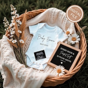 May include: A white baby onesie with the text "Baby Emma MAY 2025" and a sonogram image, inside a woven basket with flowers. A small framed sign reads "EVERY GOOD & Perfect Gift IS FROM ABOVE JAMES 1:17".