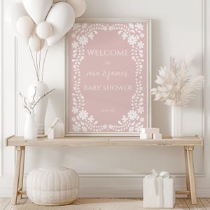 May include: A pink baby shower sign with a white floral border. The sign says "Welcome to Mia & James Baby Shower" with a date.