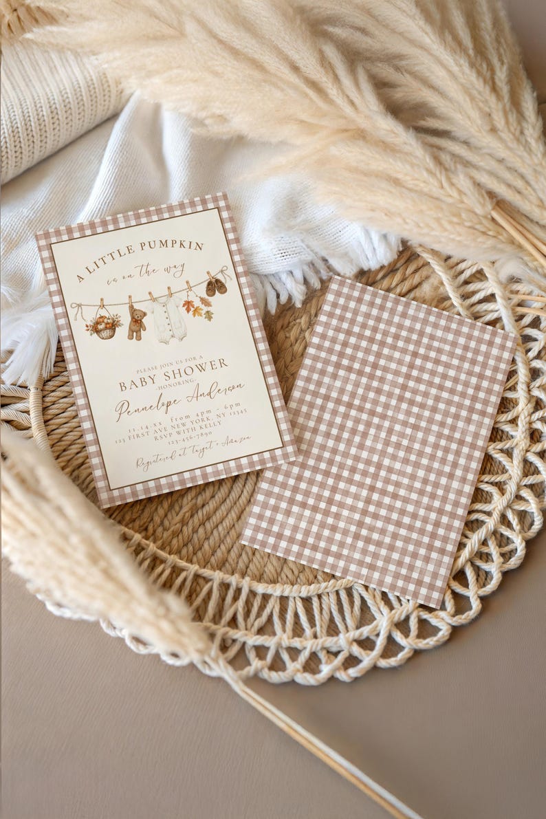 May include: A rectangular baby shower invitation card with a brown gingham border, featuring the text A LITTLE PUMPKIN is on the way, a clothesline illustration with a teddy bear, baby clothes, and autumn leaves, and a matching brown gingham card.