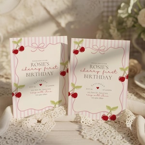 Puede incluir: Dos invitaciones de cumpleaños con fondo a rayas rosas e ilustraciones de cerezas. El texto dice "Rosie's cherry first birthday" con detalles del evento. Las invitaciones están sobre una superficie de encaje blanco.