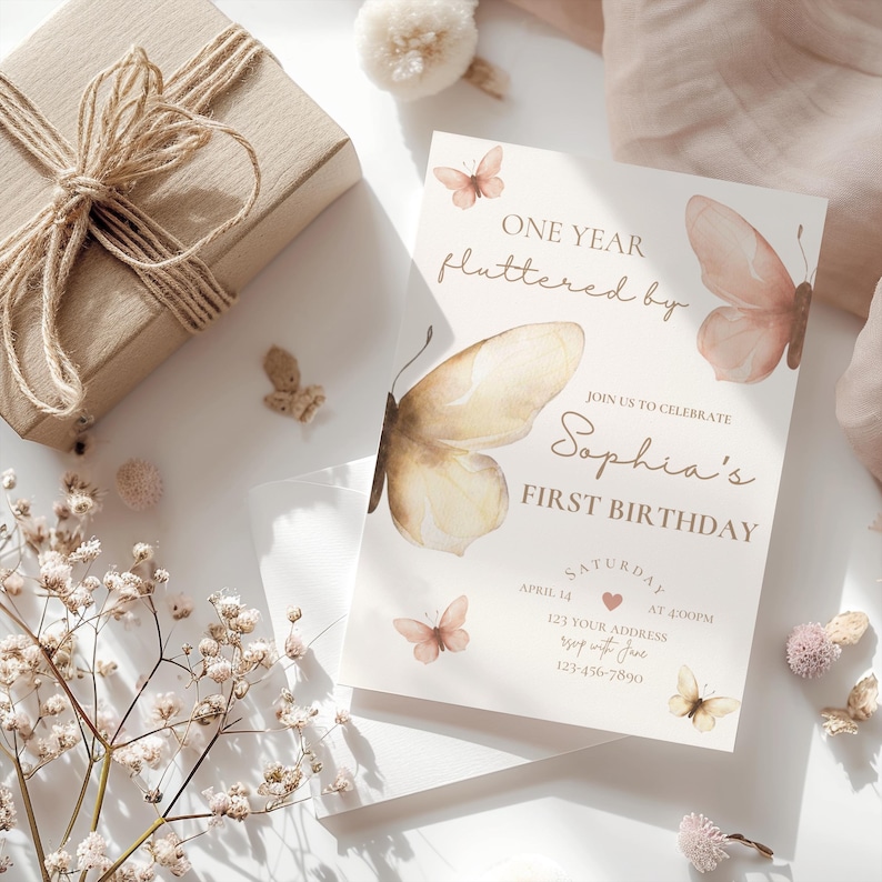 May include: A birthday invitation with butterfly illustrations and the text "ONE YEAR fluttered by Sophia's FIRST BIRTHDAY." The invitation is light beige with watercolor butterflies. A wrapped gift box and floral accents are also present.