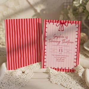 May include: Pink and red striped invitation card with the text "Sophia is Turning Thirteen." The invitation has a decorative border and a bow at the top. The back of the card has vertical red and pink stripes.