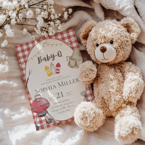 Op de afbeelding: Een rood-wit geblokte babyshower-uitnodiging met de tekst "Baby-Q" en "Sophia Miller". De uitnodiging bevat ook een grill, een fles ketchup, een fles mosterd en een babyfles. De uitnodiging is op een witte achtergrond met een teddybeer.