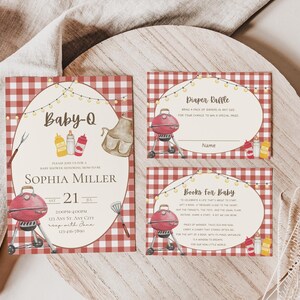 Op de afbeelding: Rode en witte gingham-gepatroneerde babyborrel-uitnodigingskaarten met een rode grill, mosterdflessen en een bruine schort. De tekst op de kaarten luidt "Baby-Q", "Sophia Miller", "21", "Luierspel" en "Boeken voor baby".
