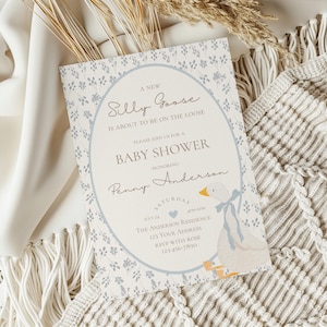 May include: A baby shower invitation with a blue and white floral pattern. The invitation features a cartoon goose with a blue bow and the text "A New Silly Goose is About to Be on the Loose".