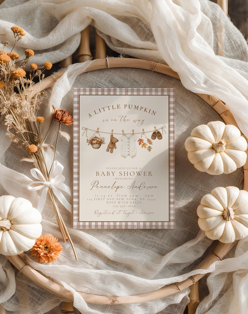 May include: A rectangular baby shower invitation card with a brown and white gingham border. The text reads A LITTLE PUMPKIN is on the way, BABY SHOWER, and HONORING PENNELOPE ANDERSON. It features illustrations of a basket, teddy bear, onesie, and leaves.