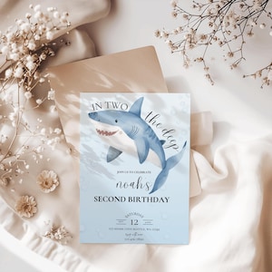 May include: A blue and white birthday invitation with a cartoon shark swimming in the ocean. The invitation says "In Two the Deep" and "Noah's Second Birthday". The date and time of the party are listed as "Saturday, Sept 12, 4pm" and the location is "121 Shark Cove Seattle, WA 12345". The phone number is 123-456-7890.