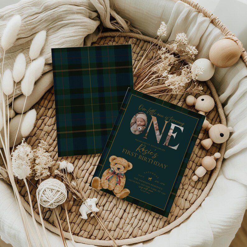 Puede incluir: Una invitaci&oacute;n de primer cumplea&ntilde;os de color verde azulado oscuro con detalles dorados y una ilustraci&oacute;n de oso de peluche. La invitaci&oacute;n incluye el texto "Our little one is turning ONE" y "Rosie's First Birthday". Tambi&eacute;n hay una tarjeta a cuadros a juego.