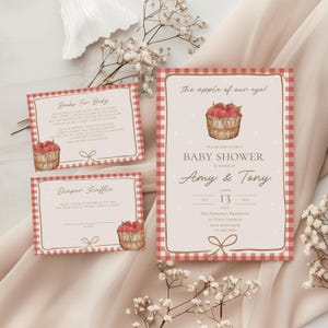 May include: A baby shower invitation set featuring a red and white gingham border, white polka dots on a cream background, and a watercolor illustration of a wooden basket filled with red apples. The text includes "The apple of our eye!", "Books For Baby", and "Diaper Raffle" with event details for Amy and Tony.