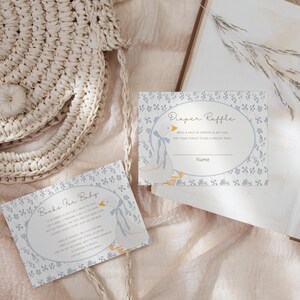 May include: Two baby shower game cards with a blue and white floral pattern. The first card says "Books for Baby" and the second card says "Diaper Raffle".