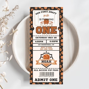 Puede incluir: Una invitación a una fiesta de primer cumpleaños con temática de baloncesto con un diseño de boleto. La invitación presenta un aro de baloncesto con una pelota de baloncesto, las palabras "Our First Draft", "Pick", "Is Turning", "One", "Saturday May 28", "4:00PM", "6:00PM", "123 Basketball St", "RSVP to Mom", "123-456-7890", "Noah", "All Access VIP Pass" y "Admit One".