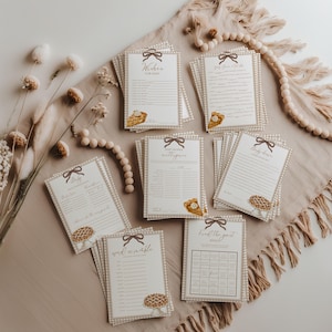 Puede incluir: Una colección de tarjetas de juegos para baby shower con un borde de cuadros vichy marrón, una ilustración de lazo marrón en la parte superior y un gráfico de pastel en la parte inferior. Las tarjetas incluyen títulos como Wishes for Baby, Baby Shower Mad Libs, Baby Predictions, Word Scramble y Find the Guest Bingo.