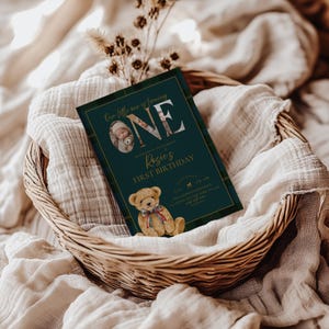 Puede incluir: Una invitaci&oacute;n de primer cumplea&ntilde;os verde oscuro con detalles dorados y un dise&ntilde;o a cuadros. La invitaci&oacute;n presenta el texto "ONE" y "Rosie's FIRST BIRTHDAY", junto con una ilustraci&oacute;n de un oso de peluche. La invitaci&oacute;n est&aacute; en una cesta tejida.