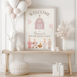 May include: A framed sign with the words "WELCOME" and "Rosie's 3rd BIRTHDAY PARTY" above cartoon farm animals. The sign is on a wooden table with balloons, vases, and a gift box. The color scheme is soft pink and white.