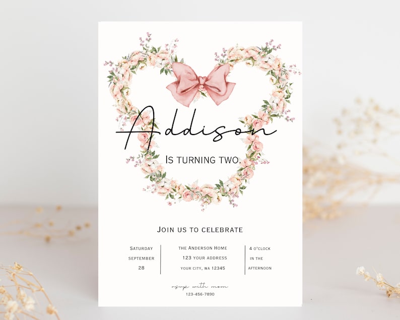 Op de afbeelding: Een roze bloemenkrans met een roze strik in het midden, met de naam "Addison" en de tekst "Is turning two." De uitnodiging bevat ook details voor een verjaardagsfeest, inclusief de datum, tijd en locatie.