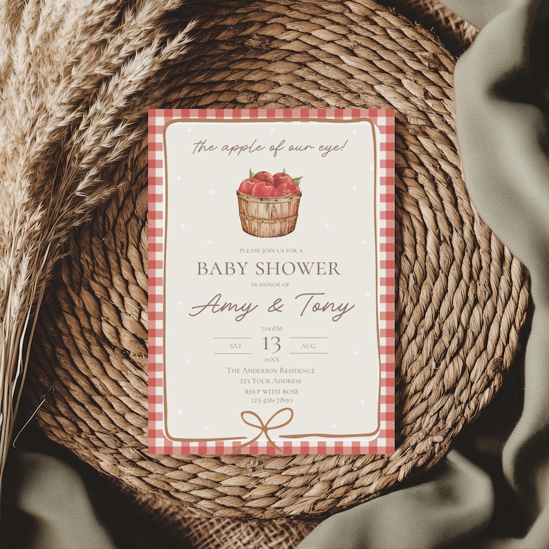 May include: Baby shower invitation with a red and white gingham border. The invitation features the text "The apple of our eye!" and includes a basket of red apples. The invitation is for Amy & Tony.