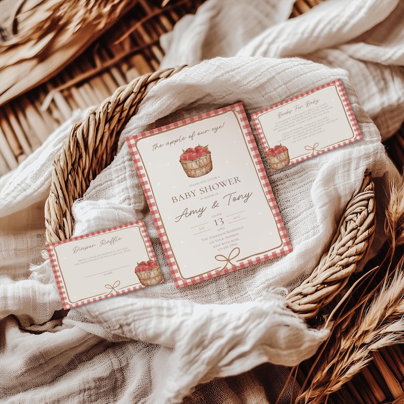 May include: A set of three printed paper cards for a baby shower featuring a red and white gingham border, a basket of apples illustration, and the text The apple of our eye, Baby Shower, Amy & Tony, Diaper Raffle, and Books For Baby.