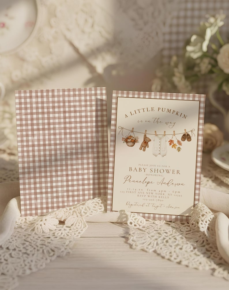 May include: A baby shower invitation card featuring a brown and white gingham border and a central illustration of a clothesline with a teddy bear, baby onesie, and autumn leaves. The text reads A LITTLE PUMPKIN is on the way BABY SHOWER.
