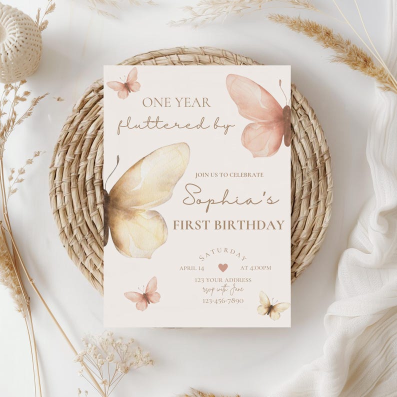 May include: A birthday invitation card with a butterfly theme. The card features the text "ONE YEAR fluttered by" and "Sophia's FIRST BIRTHDAY". The design includes watercolor butterflies in shades of peach and cream, with additional details.