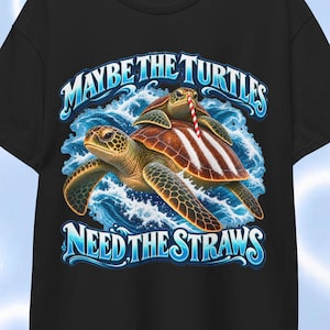 May include: A black short-sleeve t-shirt featuring a graphic of two sea turtles swimming in blue ocean waves. The top turtle has a red and white striped straw on its back. The text reads MAYBE THE TURTLES NEED THE STRAWS in blue lettering.