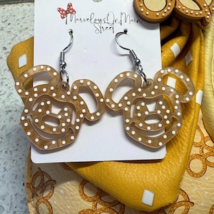 May include: A pair of brown and white Mickey Mouse-shaped earrings with white polka dots. The earrings are made of acrylic and have silver hooks.