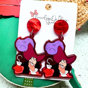 May include: Red and purple acrylic earrings featuring a cartoon image of Captain Hook from the Disney movie Peter Pan. The earrings have red and white marbled tops.