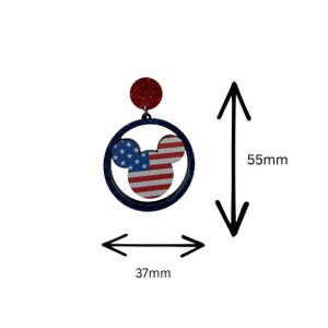 May include: A pair of patriotic earrings featuring a Mickey Mouse head design with the American flag. The earrings are approximately 2.2 inches long and 1.5 inches wide. The top is a red glitter circle, and the frame is dark blue.