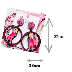 Peut inclure: Boucles d'oreilles pendantes en paillettes roses avec un personnage de cochon de dessin anim&eacute; portant une robe rose et des gants bleus. Les boucles d'oreilles mesurent 5,7 cm de haut et 3,8 cm de large.