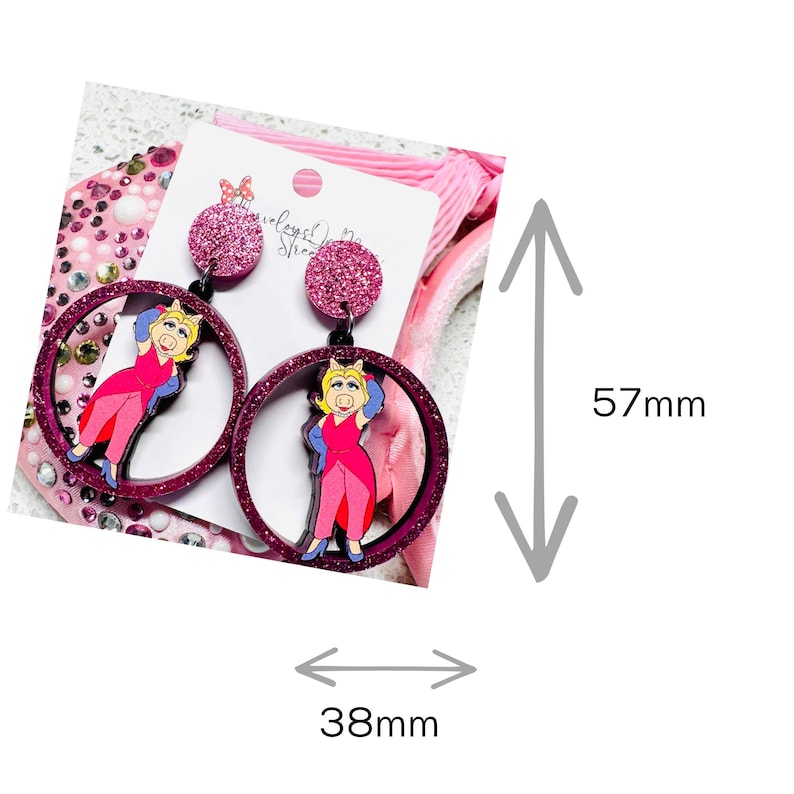 Peut inclure: Boucles d'oreilles pendantes en paillettes roses avec un personnage de cochon de dessin anim&eacute; portant une robe rose et des gants bleus. Les boucles d'oreilles mesurent 5,7 cm de haut et 3,8 cm de large.