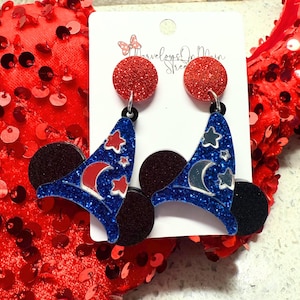 May include: A pair of blue and black glitter earrings with a Mickey Mouse ear design and a wizard hat with stars and a crescent moon. The earrings are hanging from red glitter circles.