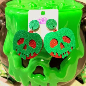 May include: A pair of green and red glitter apple earrings with a skull design. The earrings are shaped like a heart and have a dripping effect.