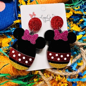 May include: A pair of black and red glitter Mickey Mouse earrings with pink glitter bows. The earrings are on a white card with the text "Treasures On Main Street".