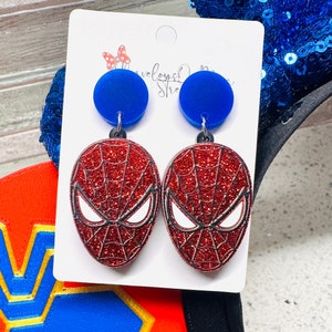 May include: Red and black glitter Spider-Man earrings with blue round accents. The earrings are on a white card with the text "Novelsy Designs Studio".