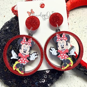 May include: Red glitter Minnie Mouse earrings. Each earring features a red glitter circle with a Minnie Mouse figure inside. The Minnie Mouse figure is wearing a red dress with white polka dots and a matching bow. The earrings are attached to a red glitter circle stud.
