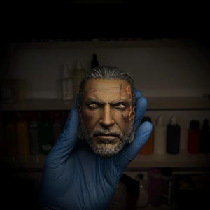 Puede incluir: Busto detallado de un hombre con expresión severa, cabello canoso y barba completa. La figura tiene cicatrices visibles en la cara y una mirada concentrada. El busto se sostiene en una mano enguantada de azul, con un fondo borroso de estantes y botellas.