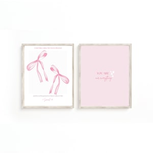Op de afbeelding: Twee ingelijste prints met een lichte houten afwerking. Eén heeft twee roze aquarel strikken met de tekst "FOR THIS CHILD WE HAVE PRAYED" en "and the Lord has granted us what we asked of Him. 1 Samuel 1:27". De andere print is roze met de tekst "YOU ARE our everything".