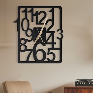 Puede incluir: Reloj de pared de metal negro con números grandes y superpuestos. El reloj tiene una aguja de hora y minutos de color dorado.