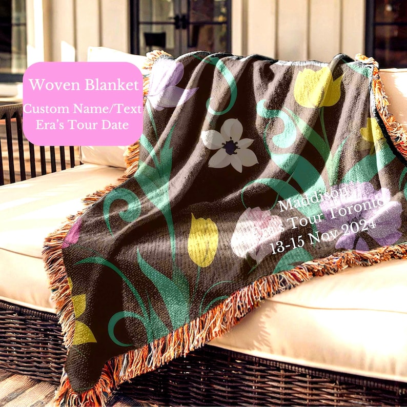 May include: A woven blanket with a brown background and a floral pattern featuring tulips, anemones, and leaves. The blanket has a fringe border and the text "Madison Tour Toronto 13-15 Nov 2024" is printed on the blanket.