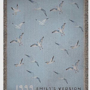 May include: A blue woven tapestry with a white fringe border. The tapestry features a repeating pattern of white seagulls flying against a light blue background. The text "1999 EMILY'S VERSION" is printed in black at the bottom of the tapestry.