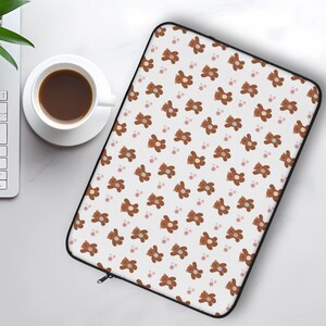 May include: A white laptop sleeve with a repeating pattern of brown teddy bears and pastel pink and blue flowers.