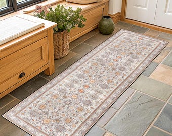 May include: A rectangular, cream-colored runner rug with an intricate, muted pattern. The rug features a border in shades of brown and a black edge. The design includes geometric and floral elements in beige, orange, and gray.