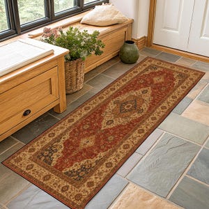 May include: A rectangular runner rug featuring a traditional ornate pattern in shades of deep red, beige, and dark blue. The rug has a detailed central medallion and a decorative border, laid flat on a stone floor with a dark, thin edge binding.