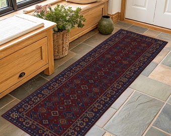 Puede incluir: Una alfombra larga y rectangular con un fondo rojo oscuro y intrincados patrones geométricos en azul y beige. La alfombra tiene un borde azul oscuro y está colocada sobre un suelo embaldosado.