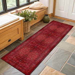 Könnte beinhalten: Ein langer, rechteckiger roter Teppich mit einem komplizierten Blumenmuster. Der Teppich liegt auf einem gefliesten Boden, und das Design weist ein zentrales Medaillon und sich wiederholende Blumenmotive auf. Die satte rote Farbe des Teppichs verleiht dem Eingang Wärme.