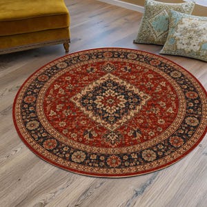 May include: A round area rug featuring a deep red background with a central navy blue and cream diamond-shaped floral medallion. The rug is bordered by a dark navy blue band decorated with repeating floral motifs in red, cream, and tan colours.