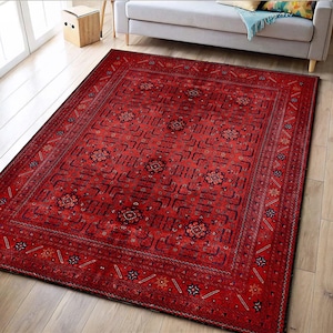 Puede incluir: Una alfombra roja rectangular con un intrincado patrón geométrico. La alfombra presenta un campo central con formas repetidas y motivos florales, enmarcado por un borde detallado. La paleta de colores incluye tonos de rojo, negro y toques de azul y dorado.