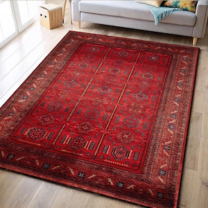 Peut inclure: Un tapis rectangulaire rouge avec un motif géométrique complexe. Le tapis présente un champ central rouge avec des formes répétées et une bordure détaillée dans des tons de marron et de bleu. Il est posé sur un sol en bois clair.