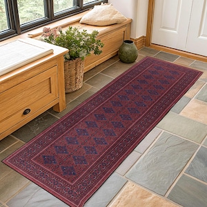 May include: A long, rectangular runner rug with a deep red background and a repeating pattern of blue diamond shapes. The rug has a detailed border and is placed on a tiled floor, suitable for a hallway or entryway.